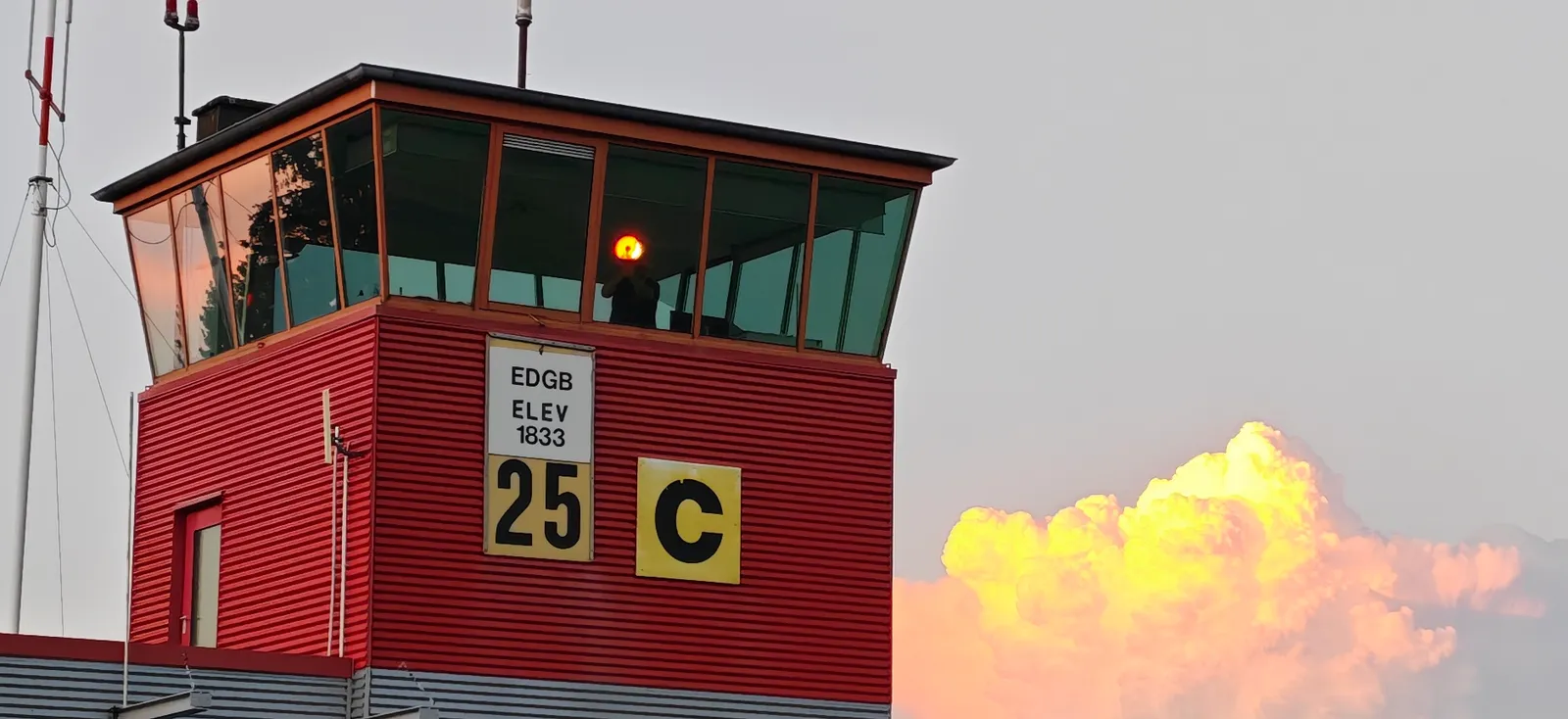 Der Kontrollturm von EDGB mit roter Verkleidung vor einer farbenprächtigen Gewitterwolke im Abendlicht